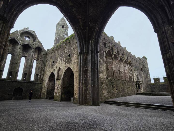 Impressive Gothic ruins of the Rock of Cashel framed by pointed arches on a grey day.