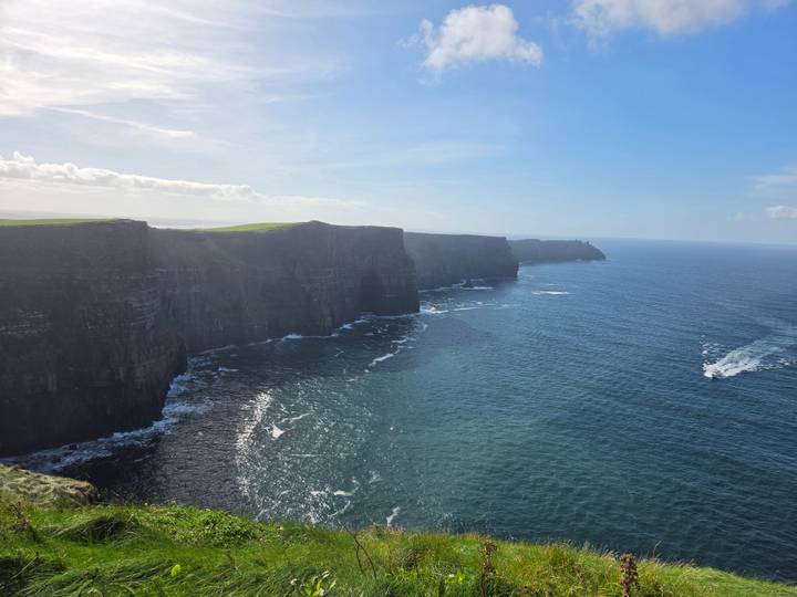 Sheer sea cliffs stretch into the distance at the famous Cliffs of Moher under blue skies.