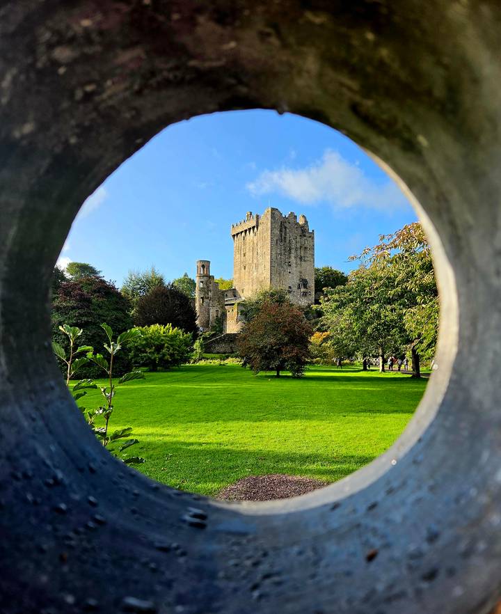 Blarney Castle framed artistically through a circular stone opening with lush grounds.