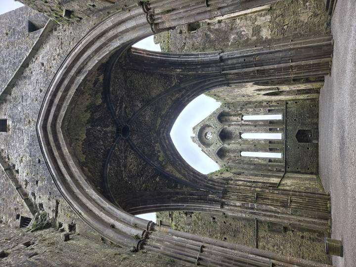 Soaring Gothic arch frames the empty nave of a ruined cathedral at the Rock of Cashel.