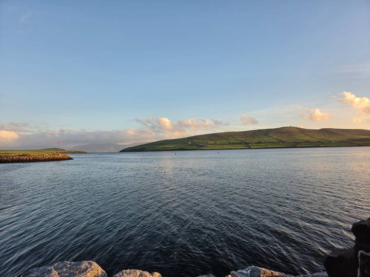 Golden evening light over calm harbour waters and rolling green hills of Dingle.