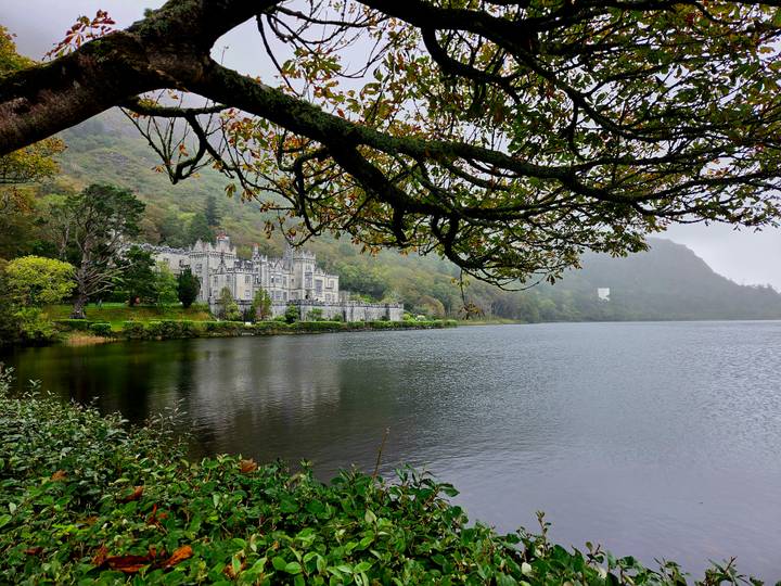 Kylemore Abbey nestles beside a reflective lake framed by overhanging autumn branches.