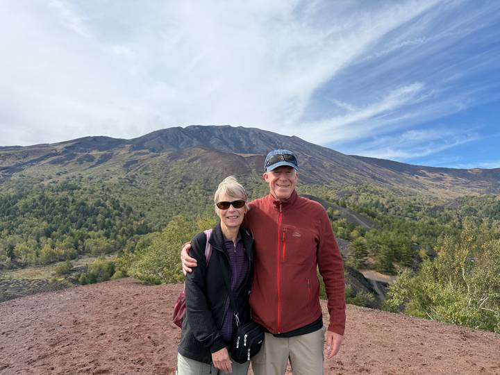 Couple standing on red volcanic soil of Mount Etna with rugged crater landscape in the background