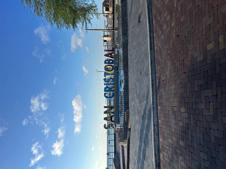 Colourful SAN CRISTOBAL sign on a waterfront promenade under a blue sky with scattered clouds.