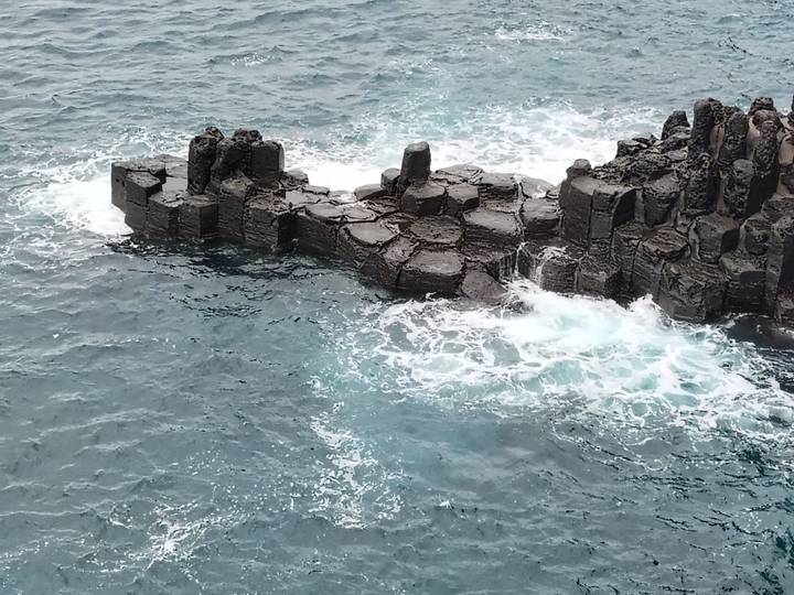Columnar basalt rock formation surrounded by turquoise ocean waves crashing against the shore.