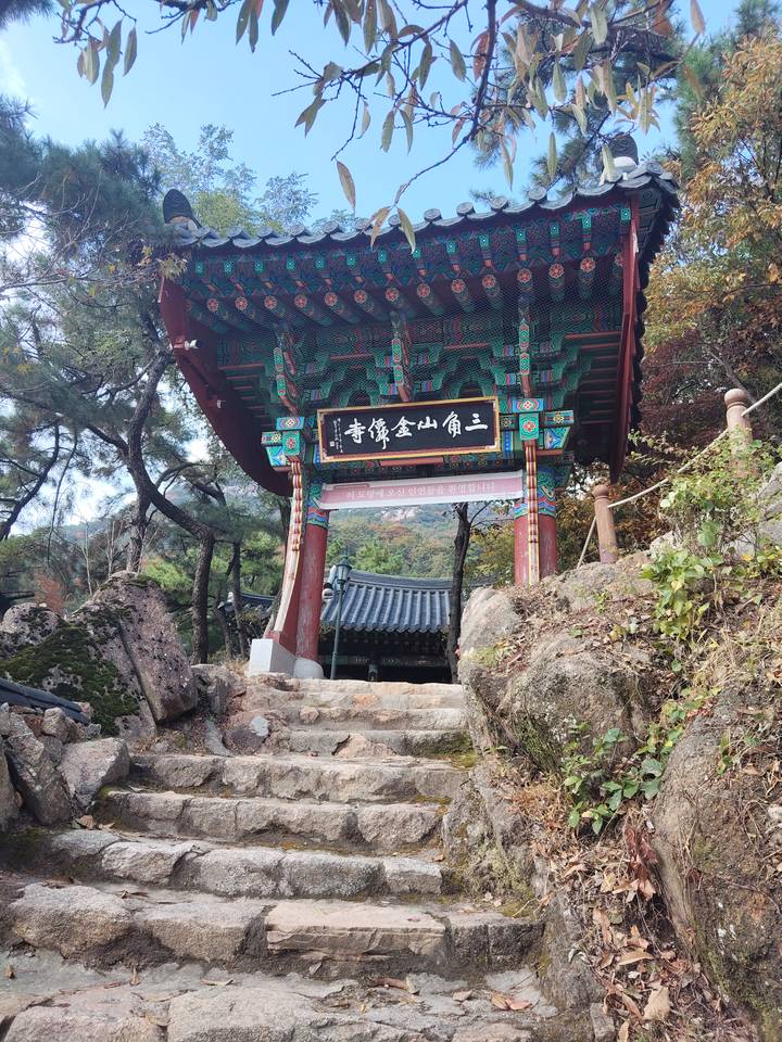 Ornate Korean temple gate painted in bright colors, framed by rocky steps and autumn forest.