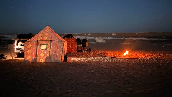 Patterned desert tent and glowing campfire beneath a starry night sky.