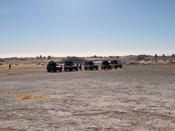 Convoy of off-road vehicles parked on the flat, sun-bleached desert plain.