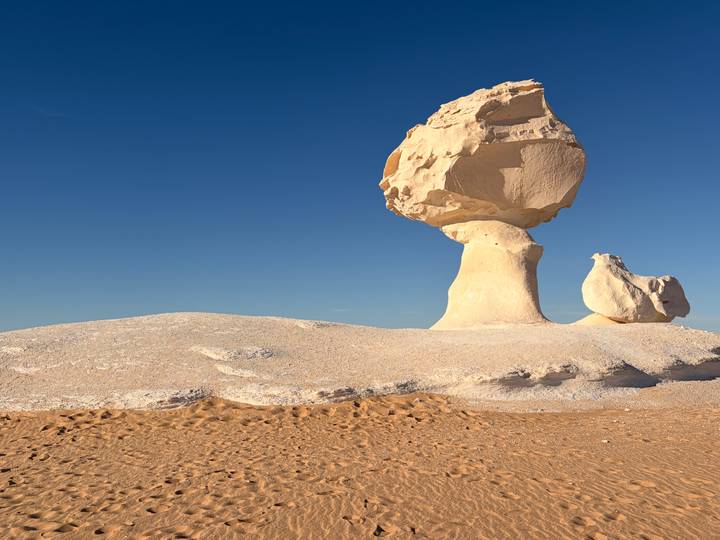 Iconic mushroom-shaped white chalk formation rising from sandy desert under deep blue sky.