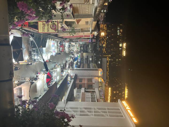 Bustling night market street lit by neon signs and rows of white canopied stalls.