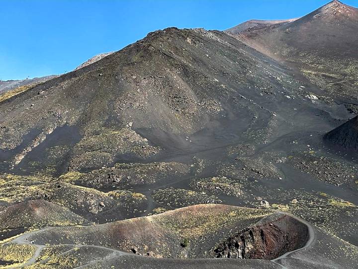 Barren dark volcanic slopes and craters of Mount Etna under a clear blue sky.