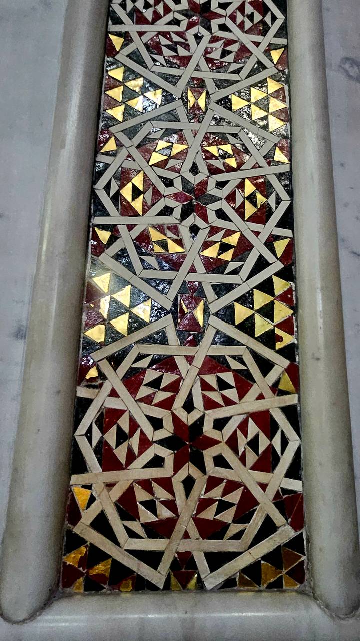 Close-up of intricate geometric inlaid mosaic with gold, red and black tiles.