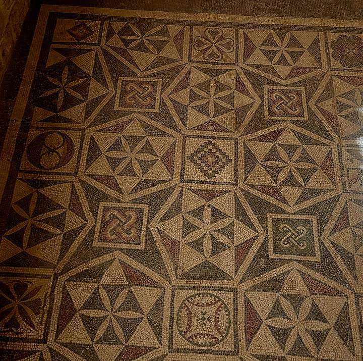 Ancient floor mosaic composed of repeating star and geometric patterns in earth tones.