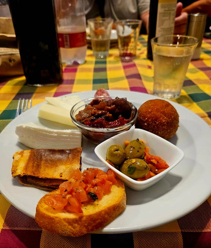 Colourful Sicilian antipasto plate with cheeses, olives, caponata and arancini on checked tablecloth.