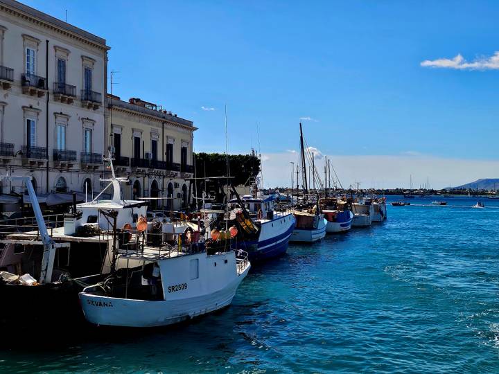 Row of small fishing boats moored along the waterfront promenade of a historic coastal city.