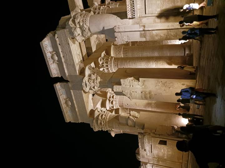 Impressive lit columns and capitals of Kom Ombo Temple at night with visitors exploring.