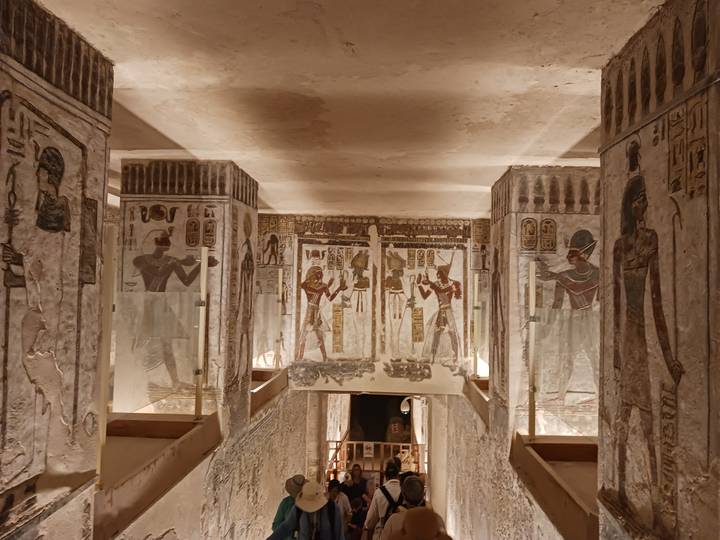 Colourful painted walls and pillars inside an ancient Egyptian tomb corridor, warmly lit.