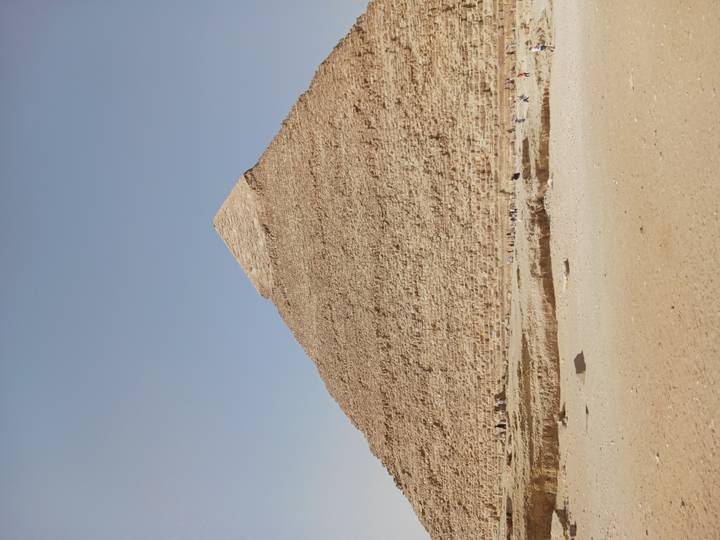 Full view of the Great Pyramid of Giza rising against a pale desert sky.