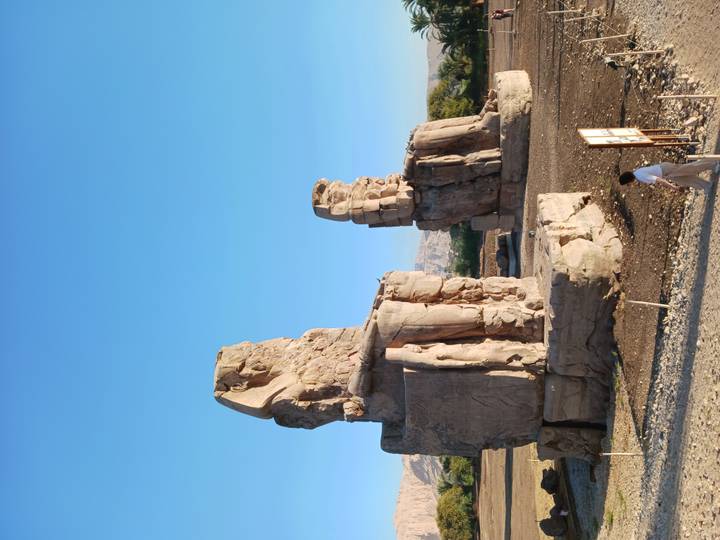 Morning light on the Colossi of Memnon statues towering over a lone visitor.