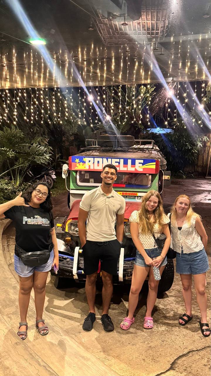 Four friends posing happily in front of a brightly painted jeepney at night.