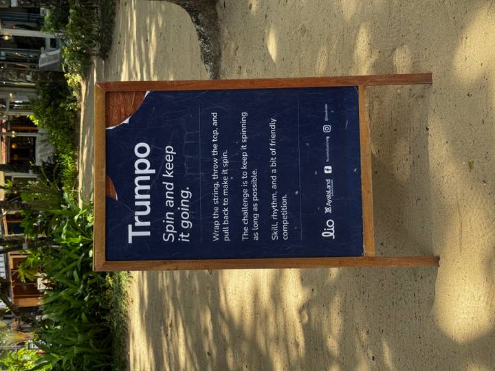 A wooden signboard explaining a Filipino spinning-top game set on a sandy pathway.