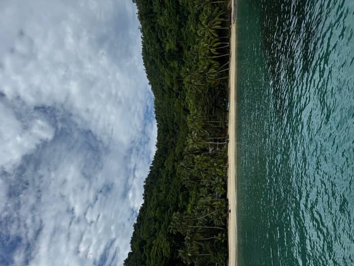 Turquoise water in front of a secluded tropical beach backed by lush green hills and palms.