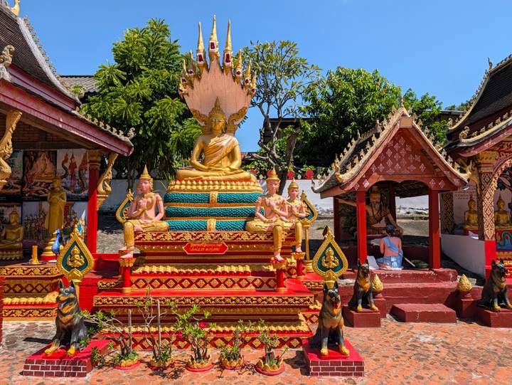 Brightly painted outdoor Buddhist shrine with golden seated Buddha against blue sky