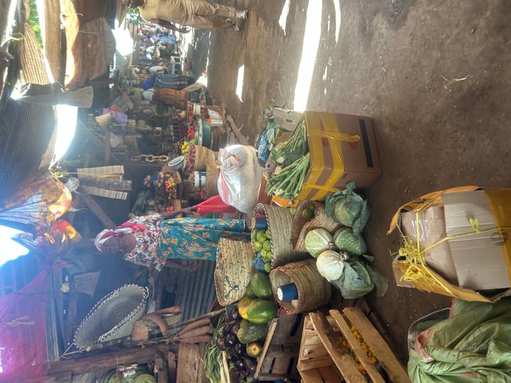 A vendor stands beside colourful baskets of produce inside a busy local market.
