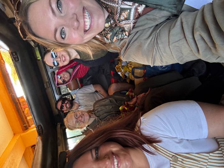 Smiling travelers take a selfie inside a safari vehicle packed with gear.