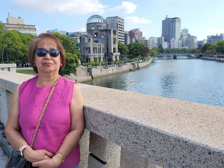 Woman in pink stands on a bridge overlooking Hiroshima’s Peace Memorial and its riverside park.