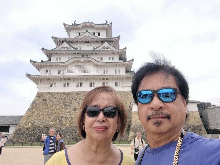 Couple selfie in front of the imposing white walls and stone base of Himeji Castle.