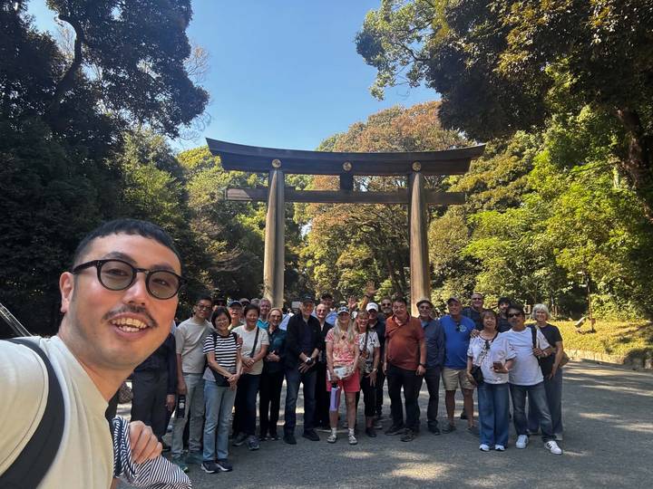 Large tour group gathers for a photo in front of a wooden torii gate surrounded by forest.