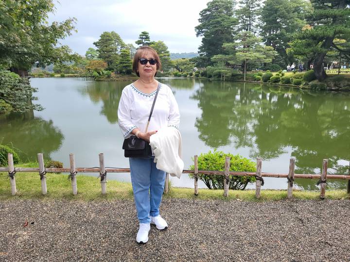 Woman poses beside a reflective pond and manicured trees in Kanazawa’s Kenrokuen Garden.