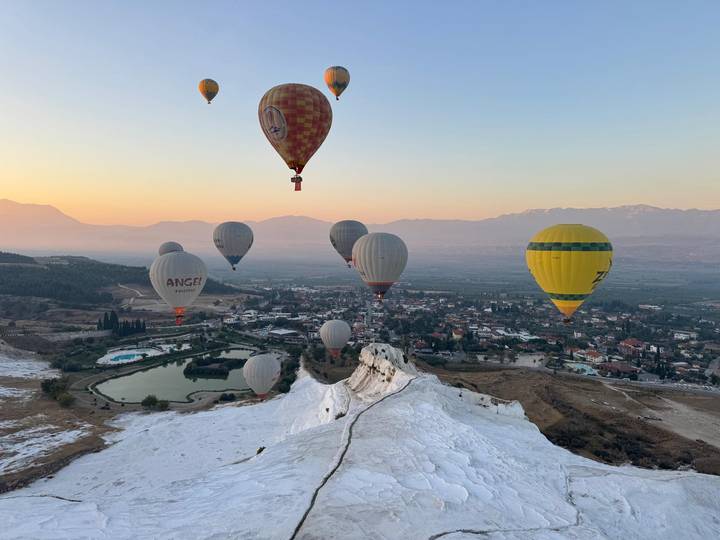 Dozens of hot-air balloons soar over Pamukkale’s white travertine terraces at sunrise.
