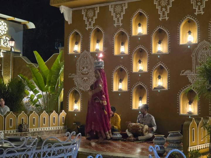 A traditional Rajasthani dancer balances pots on her head while musicians play in a lantern-lit courtyard.
