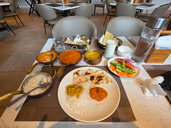 A table set with an array of North Indian curries, rice, breads, and fresh vegetables in a modern dining room.