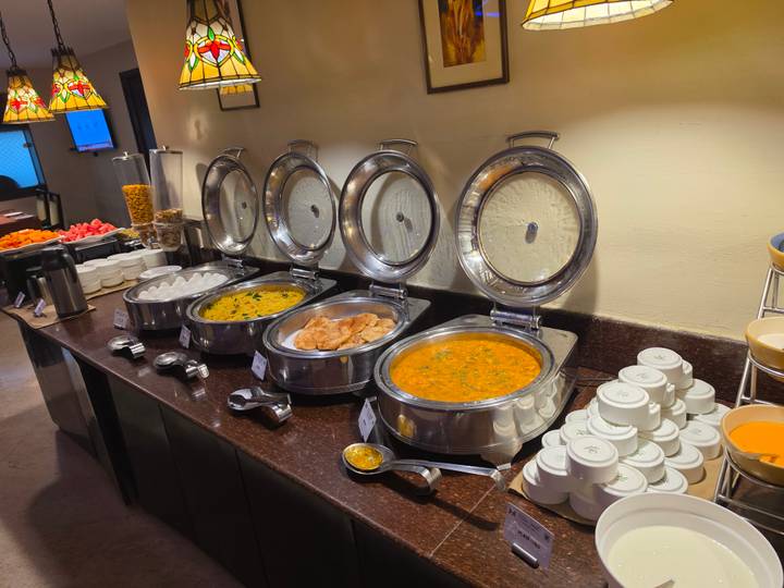 A hotel buffet with steel chafing dishes containing eggs, dal and curries alongside plates and condiments.