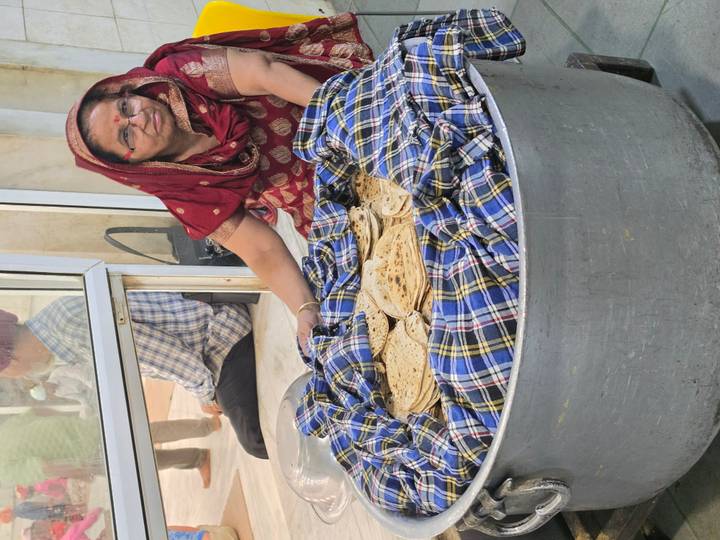 A woman in a red sari tends a huge pot filled with freshly cooked chapatis at a community kitchen.