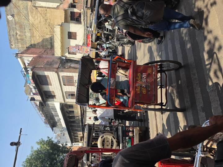 A cycle rickshaw navigates a busy street lined with shops and traffic in an Indian city.