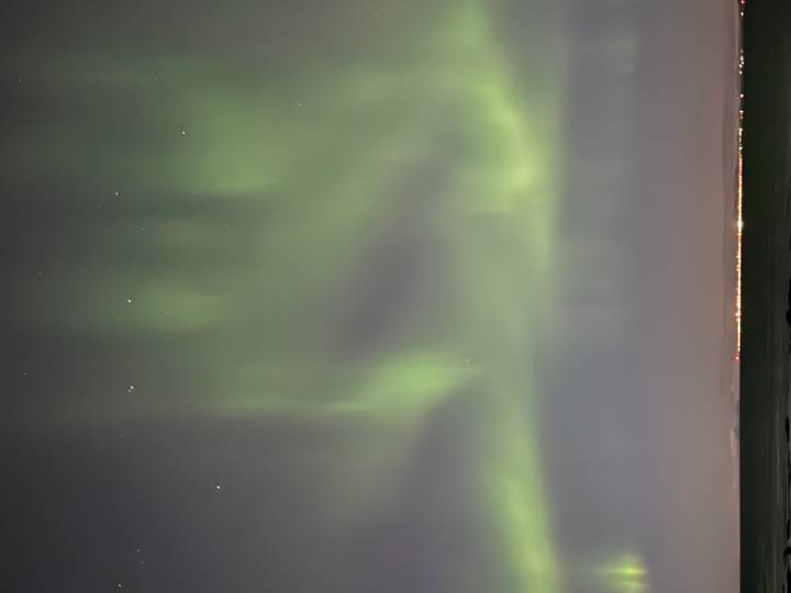 Green aurora borealis lights dancing in the night sky above a distant coastline.