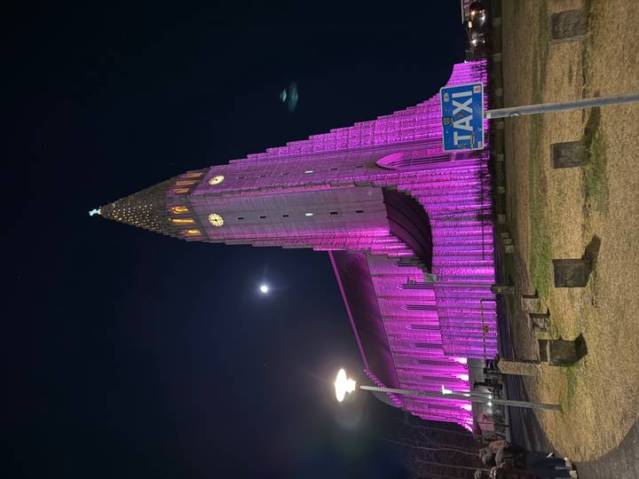 Hallgrímskirkja church illuminated in pink lights under a night sky and crescent moon.