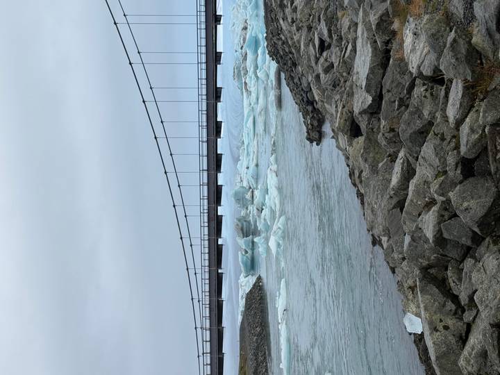 Suspension bridge spanning over glacial icebergs floating in a lagoon.