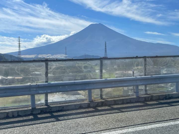 View of Mount Fuji taken from a moving vehicle behind a metal guardrail.