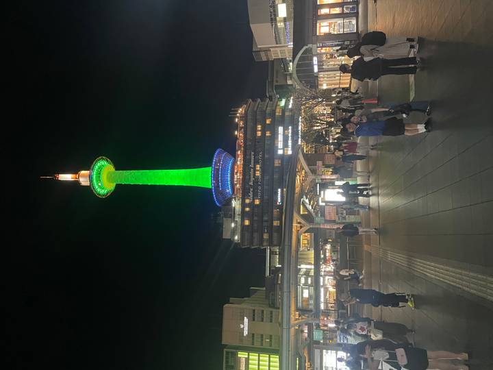 Kyoto Tower lit in bright green standing over a busy plaza at night.