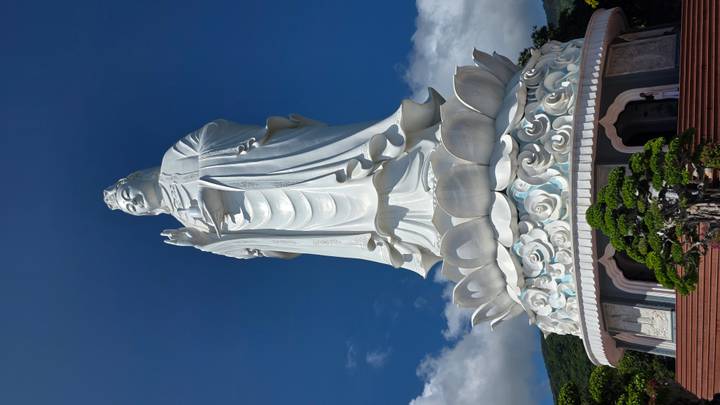 Towering white Lady Buddha statue atop a lotus pedestal under a clear blue sky