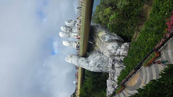 Famous Golden Bridge held by giant stone hands over green forested hills with visitors walking across