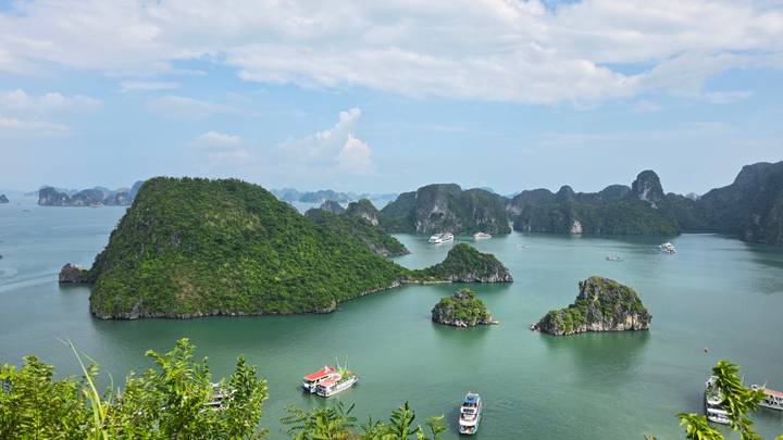 High viewpoint over green limestone islands and boats dotting turquoise Halong Bay