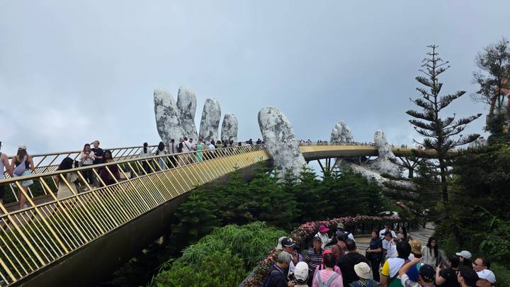 Crowds of tourists walk along the Golden Bridge’s curving span supported by giant hands