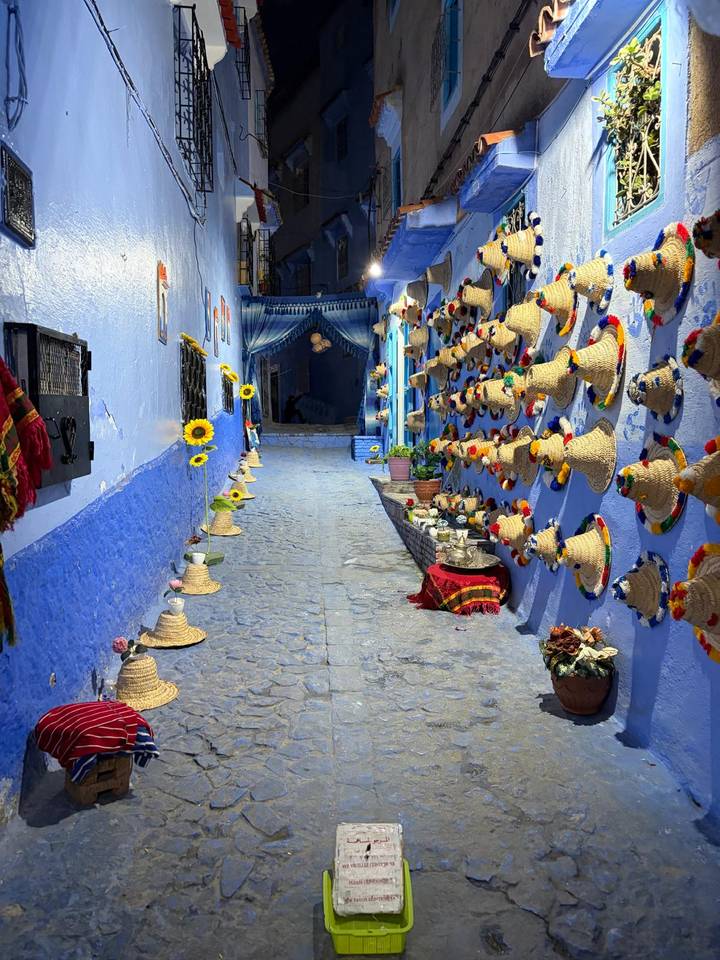 Narrow alley in Chefchaouen painted vivid blue, lined with colourful woven hats and sunflowers
