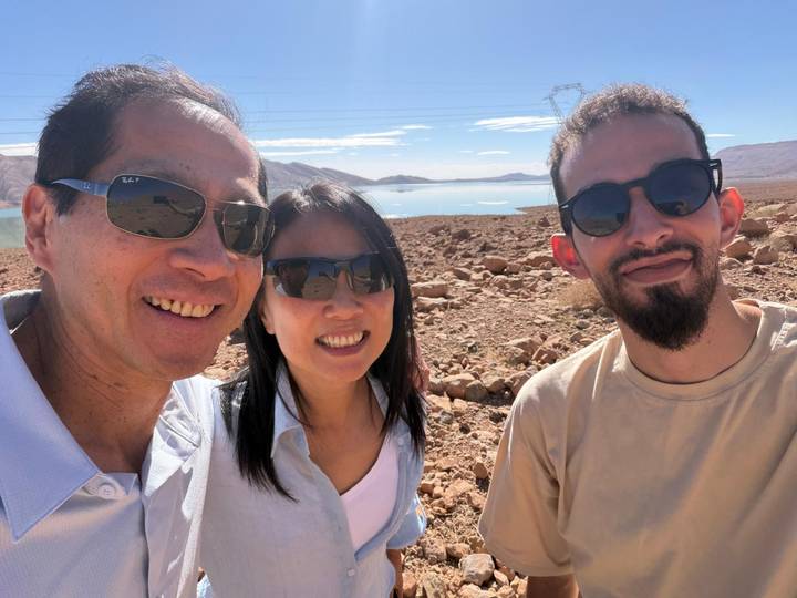 Three travellers take a selfie with arid rocky landscape and a reflective lake in the background